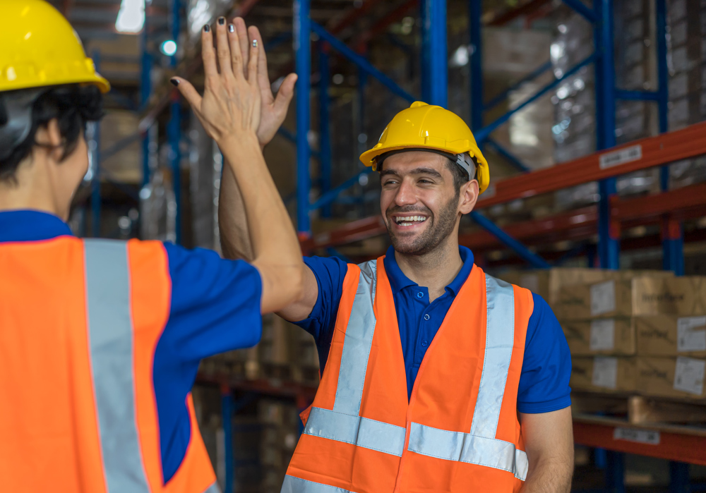 Male worker in hard hat and hi-vis high-fiving a colleague